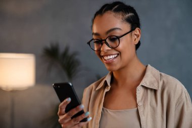 Cheerful young businesswoman using mobile phone while standing in the office