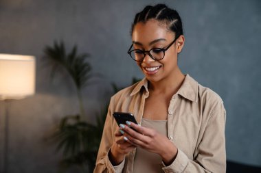 Cheerful young businesswoman using mobile phone while standing in the office