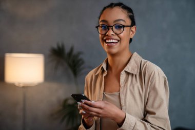 Cheerful young businesswoman using mobile phone while standing in the office
