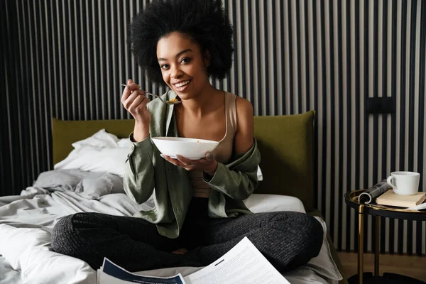 Счастливая Африканская Американская Девушка Изучает Документы Время Еды Хлопья Постели — стоковое фото
