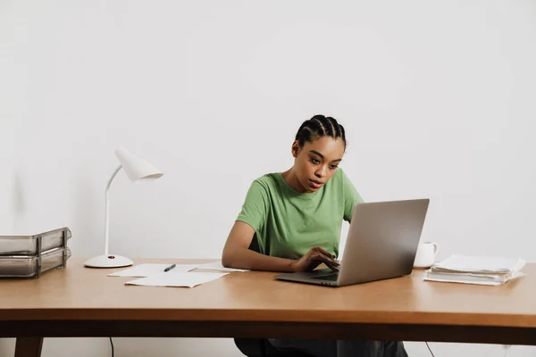 坐在办公室桌子旁 拿着笔记本电脑工作的黑人年轻女人 — 图库照片