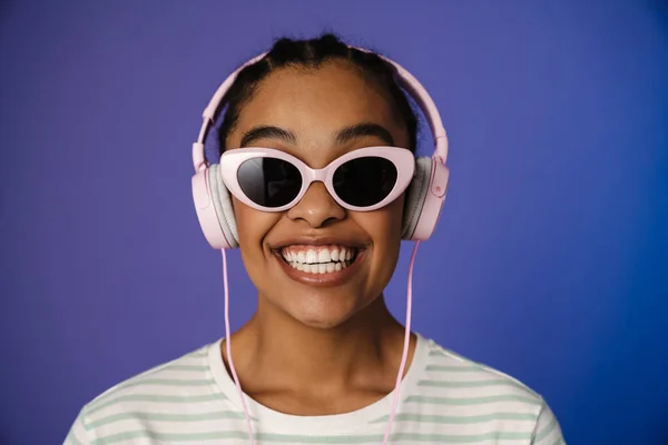 Excited black woman in headphones smiling at camera isolated over blue background