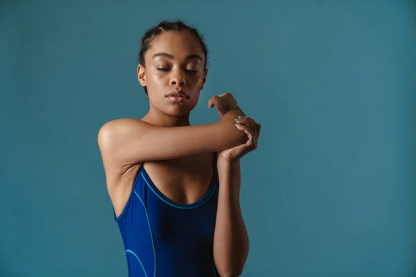 Young black swimmer doing exercise while working out isolated over blue wall