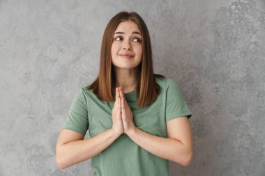 Avuç içlerini bir arada tutan mutlu, güzel bir kız. Gri duvarın diğer tarafına bakıyor.