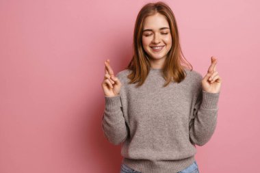 Kızıl mutlu kadın, şans dilemek için pembe arka planda poz veriyor.