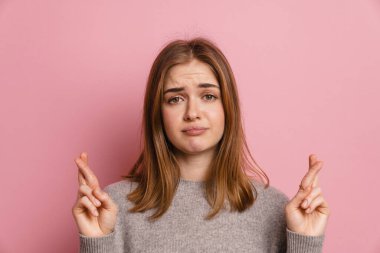 Kızıl saçlı üzgün kadın, şans dilemek için pembe arka planda poz veriyor.