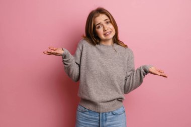 Ginger 'ın kafası karışmış bir kadın pembe arka plan üzerinde kopyalama alanını tutarken kameraya bakıyor.