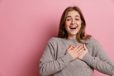 Kızıl, heyecanlı, gülümseyen bir kadın pembe arka planda el ele tutuşurken.