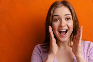 Genç kızıl heycanlı kadın turuncu duvardan izole edilmiş kameraya bakıyor ve bağırıyor.