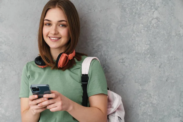 Happy Nice Student Girl Headphones Smiling Using Cellphone Isolated Grey — Stock Fotó