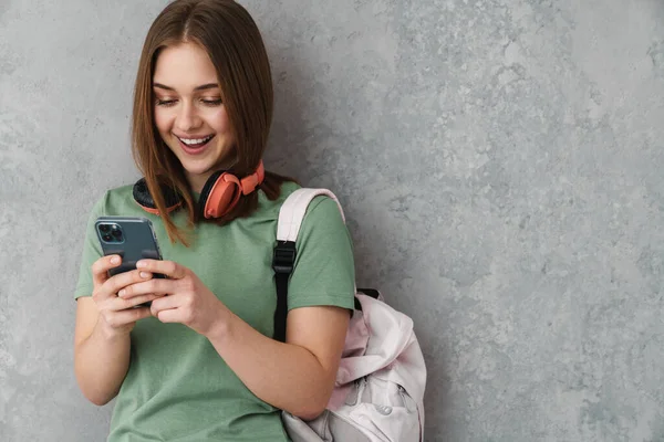 Happy Nice Student Girl Headphones Smiling Using Cellphone Isolated Grey — Stock Fotó