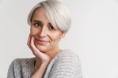 Beyaz saçlı genç kadın gülümsüyor ve beyaz duvarın üzerinden izole edilmiş kameraya bakıyor.