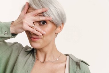 Genç, gri saçlı, gülümseyen ve yüzünü kapatan bir kadın.