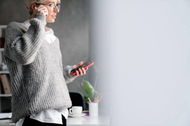 Ofiste dururken cep telefonu ve kulaklık kullanan beyaz saçlı bir kadın.