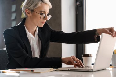 Ofiste otururken dizüstü bilgisayarla çalışan beyaz saçlı şaşkın kadın.