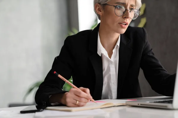 Mujer Desconcertada Pelo Blanco Escribiendo Notas Mientras Trabaja Con Ordenador — Foto de Stock