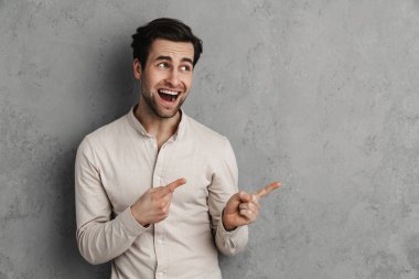 Neşeli yakışıklı adam gülümsüyor ve gri duvarın üzerinde izole edilmiş parmakları işaret ediyor.