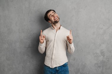 Gri arka planda izole edilmiş fotokopi alanını gösteren günlük kıyafetli, güler yüzlü çekici bir adam.