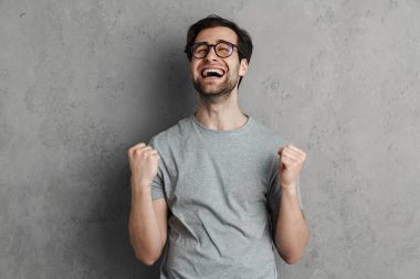 Heyecanlı yakışıklı adam çığlık atarken, kazanan jestler gri duvarda izole ediliyor.