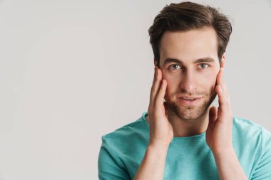 Gri arka planda izole edilmiş kameraya bakan düşünceli, çekici, sıradan bir genç adam.