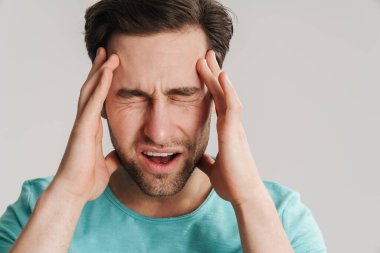 Gri arka planda izole edilmiş güçlü bir migrenden muzdarip stresli bir adam.