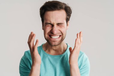 Gri arka planda izole edilmiş güçlü bir migrenden muzdarip stresli bir adam.