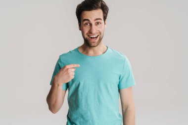 Heyecanlı yakışıklı adam gülümsüyor ve beyaz duvarın üzerinde kendini işaret ediyor.