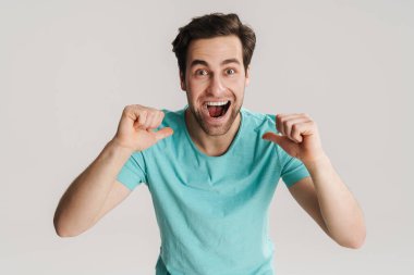 Heyecanlı yakışıklı adam gülümsüyor ve beyaz duvarın üzerinden kendini işaret ediyor.