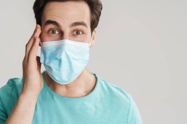 Beyaz duvarın üzerinden izole edilmiş beyaz kameraya bakan koruyucu maskeli beyaz adam.