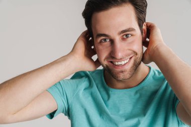 Gri arka planda izole edilmiş mutlu ve çekici genç bir adam. Yaklaş, poz ver.