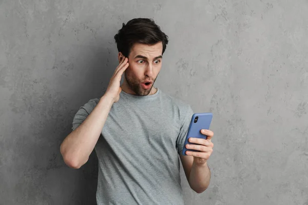 Chico Guapo Impactado Exclamando Mientras Utiliza Teléfono Móvil Aislado Sobre — Foto de Stock