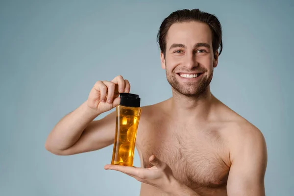 Close Smiling Handsome Young Nude Man Presenting Shampoo Bottle Isolated — ストック写真