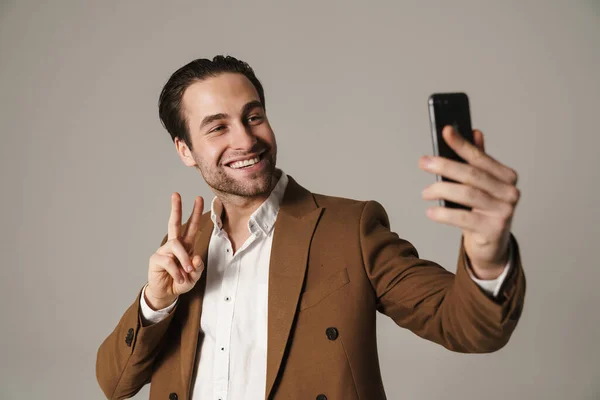Brunette Man Showing Peace Sign Taking Selfie Cellphone Isolated Grey — Stock Fotó