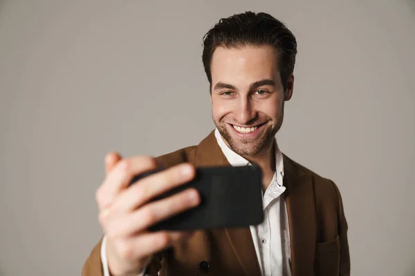 没有刮胡子的黑发男人笑着用灰色背景的手机自拍 — 图库照片