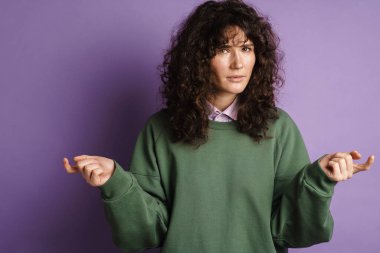 Kara kara düşünen esmer, kıvırcık kız. Mor arka planda izole edilmiş ellerle düşünüyor ve hareket ediyor.