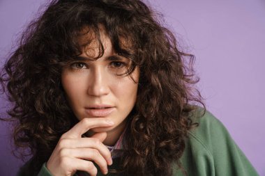 Kara kara düşünen güzel kıvırcık kız mor arka planda parmaklarıyla kameraya bakıyor.