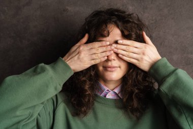 Genç, esmer, kıvırcık kız kara duvarın üzerinde elleri izole bir şekilde gözlerini kapatıyor.