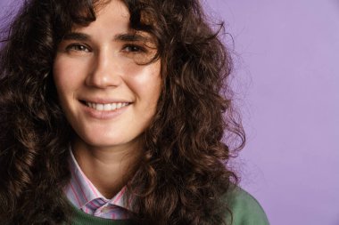 Mutlu güzel kıvırcık kız gülümsüyor ve mor arka planda izole edilmiş kameraya bakıyor.