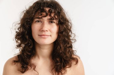 Yarı çıplak kıvırcık kadın beyaz arka planda yalnız poz veriyor ve kameraya bakıyor.