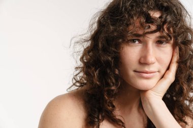 Yarı çıplak kıvırcık kadın beyaz arka planda yalnız poz veriyor ve kameraya bakıyor.