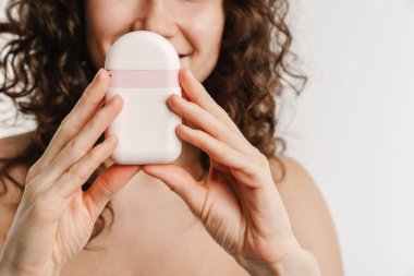 Yarı çıplak kıvırcık kadın gülümsüyor ve beyaz arka planda el kremi gösteriyor.