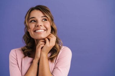 Mutlu, güzel, güzel bir kız gülümseyip, mor arka planda soyutlanmış bir kenara bakıyor.