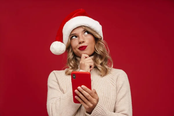 Mutlu Düşünceli Noel Baba Şapkalı Kırmızı Arka Planda Cep Telefonu — Stok fotoğraf