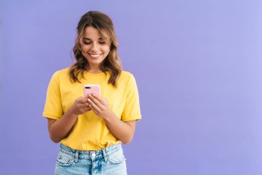 Mor arka planda izole edilmiş cep telefonu kullanırken gülümseyen mutlu güzel kız.