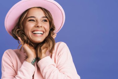 Mutlu, şapkalı, gülüp bakan, mor arka planda yalnız, sevimli bir kız.