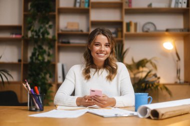 Ofisteki belgelerle uğraşırken cep telefonu kullanan çekici, genç bir girişimci.