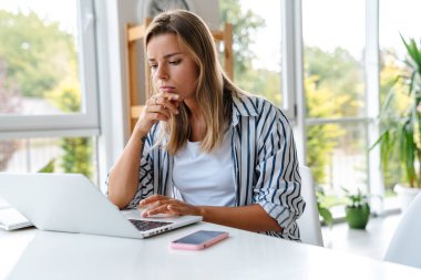 Çekici, düşünceli, kendine güvenen, yaratıcı ofiste çalışan, dizüstü bilgisayar kullanan genç bir kadın.