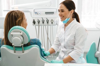 Avrupalı orta dişçi kadın dişçi kliniğinde hastayla çalışırken gülümsüyor