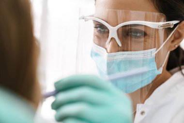 Diş kliniğinde çalışan maskeli Avrupalı orta dişçi kadın.