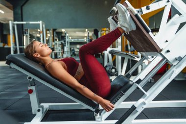 Spor salonunda bacaklar için spor yapan genç bir kadın fitness koçunun görüntüsü.